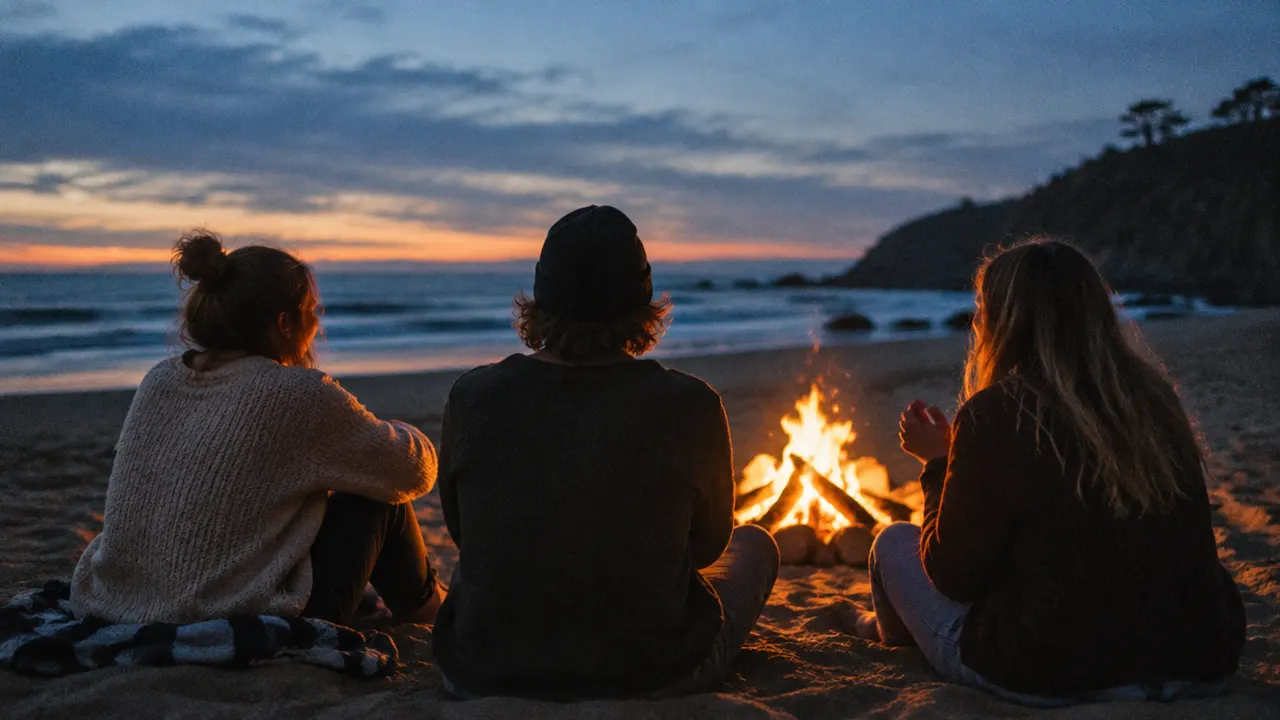 Three friends talking around a campfire on a beach at dusk
